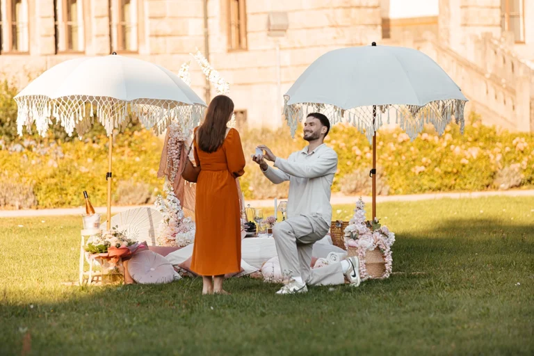 Mann macht einen romantischen Heiratsantrag auf den Knien bei einem Luxus-Picknick im Schlosspark.