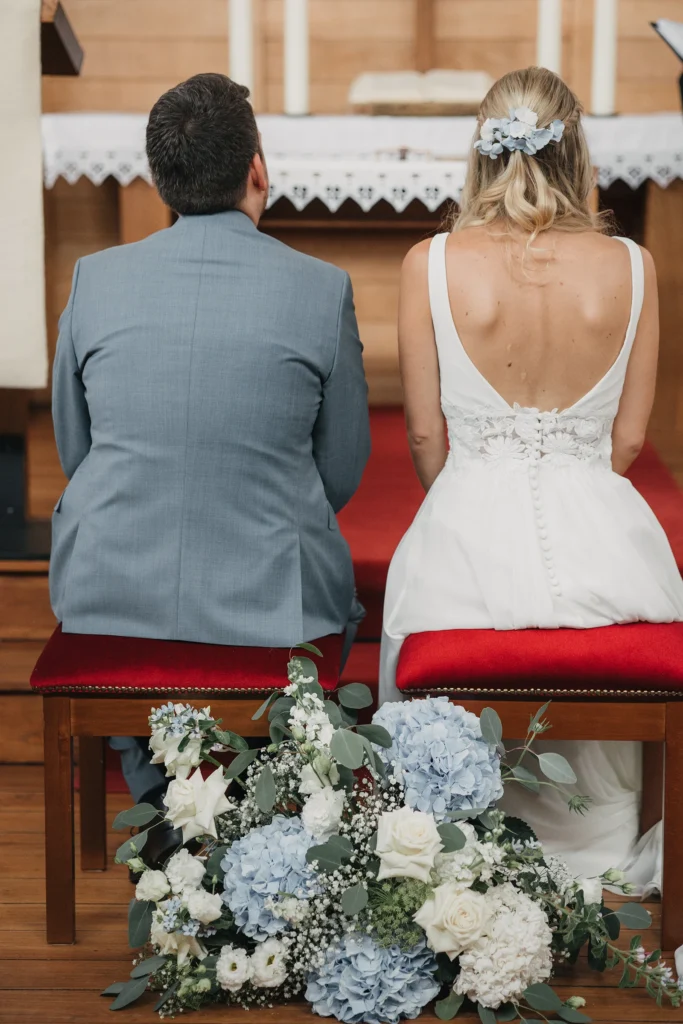 Brautpaar sitzt gemeinsam vor dem Altar, prächtige Blummenstrauß liegt vor der Bank