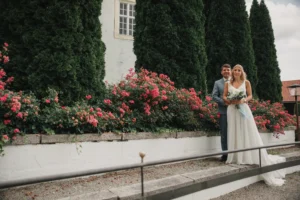 Brautpaar steht an einer Steintreppe neben roten Rosen im Schlossgarten Neufahrn