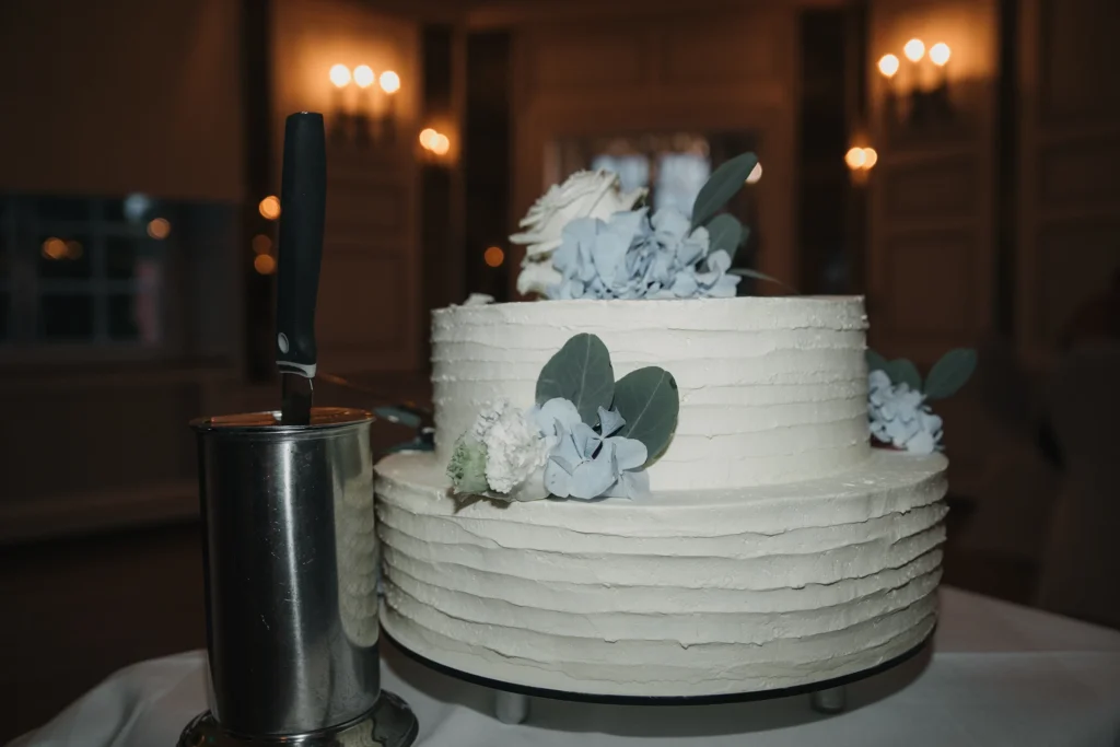 Mehrstöckige weiße Hochzeitstorte mit hellblauen Blüten und grünen Blättern