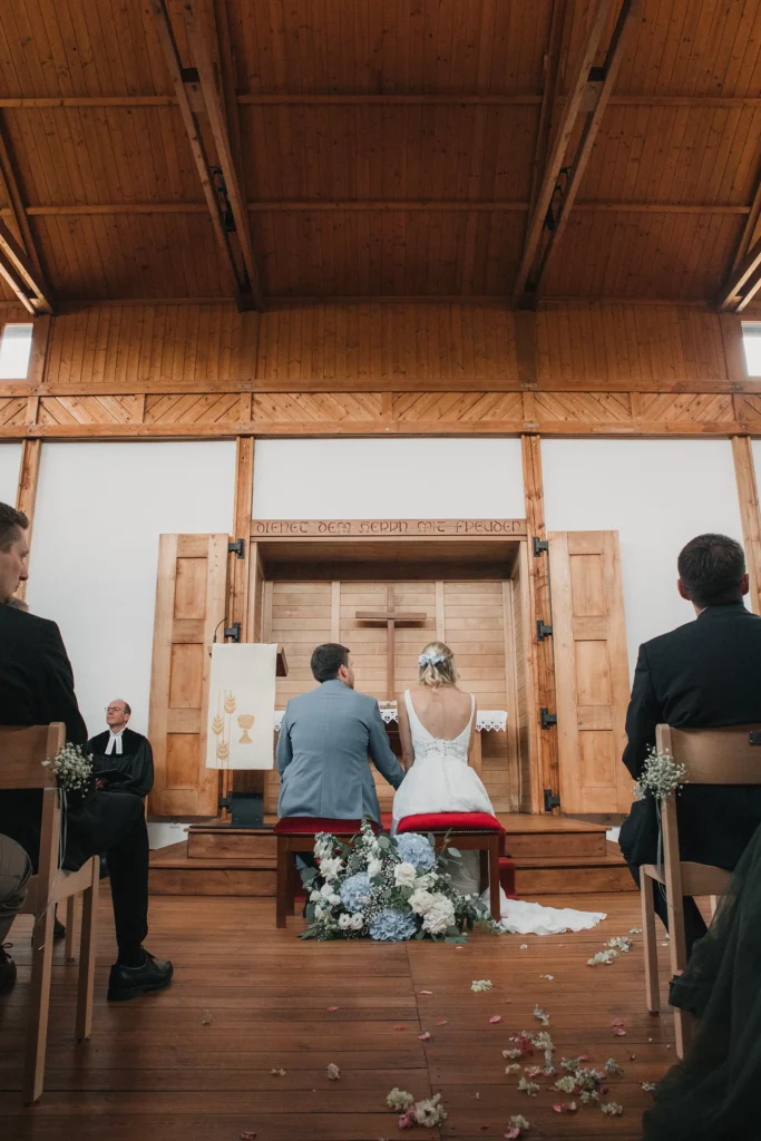 Blick durch den Kirchenraum mit Holzwänden und Holzboden auf das Brautpaar am Altar
