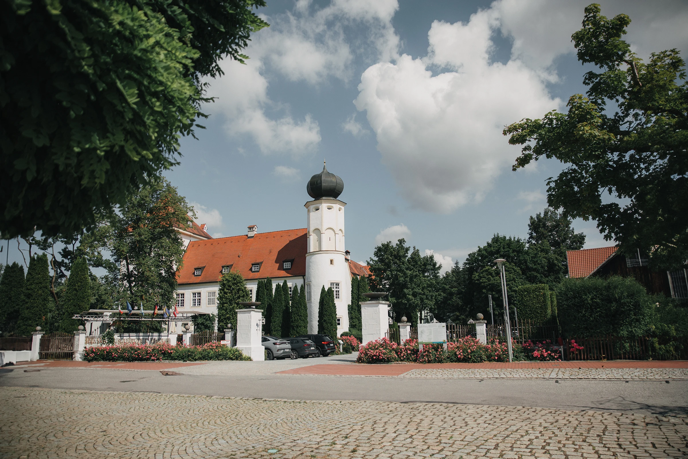 Außenansicht des Schloss-Hotels Neufahrn mit Schlossturm, Rosengarten und rotem Ziegeldach