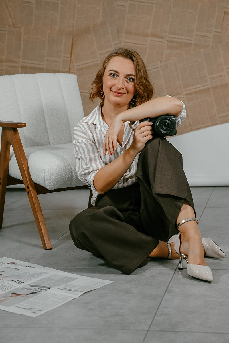 Boudoir-Fotografin Natalia Fichtner sitzt mit ihrer Kamera neben einem hellen Sessel.