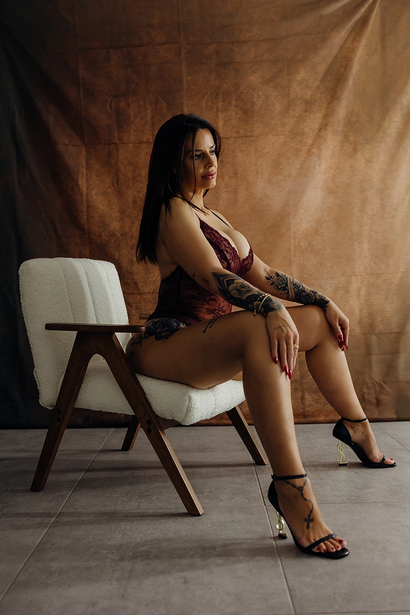 Frau sitzt bei ihrem Boudoir-Shooting in dunkler Wäsche und hohen Schuhen auf einem Holzstuhl.
