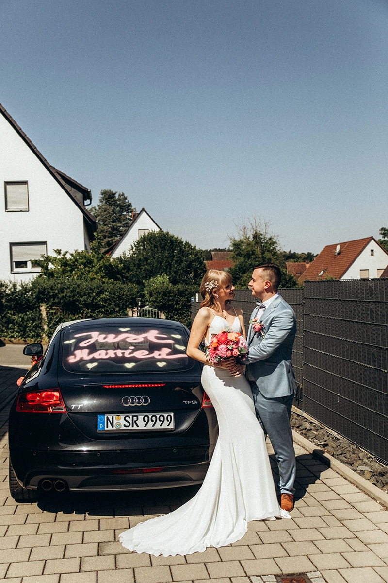 Das Brautpaar küsst sich neben dem mit „Just married“ geschmückten Hochzeitsauto.