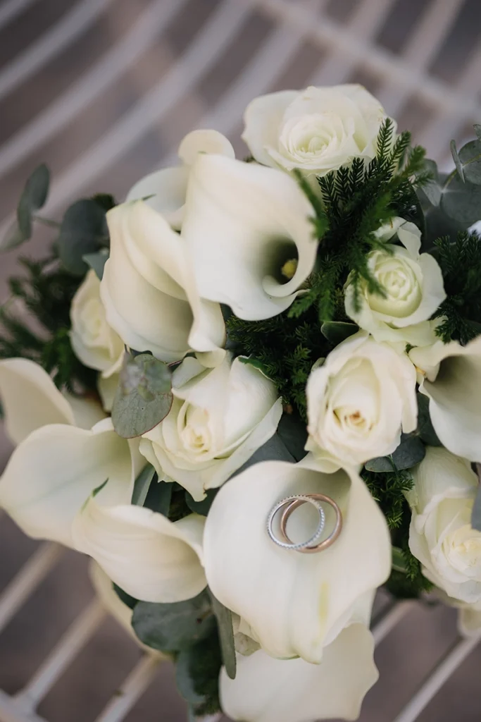 Weiße Callas und Rosen im Brautstrauß mit den beiden Eheringen auf einer Blüte.