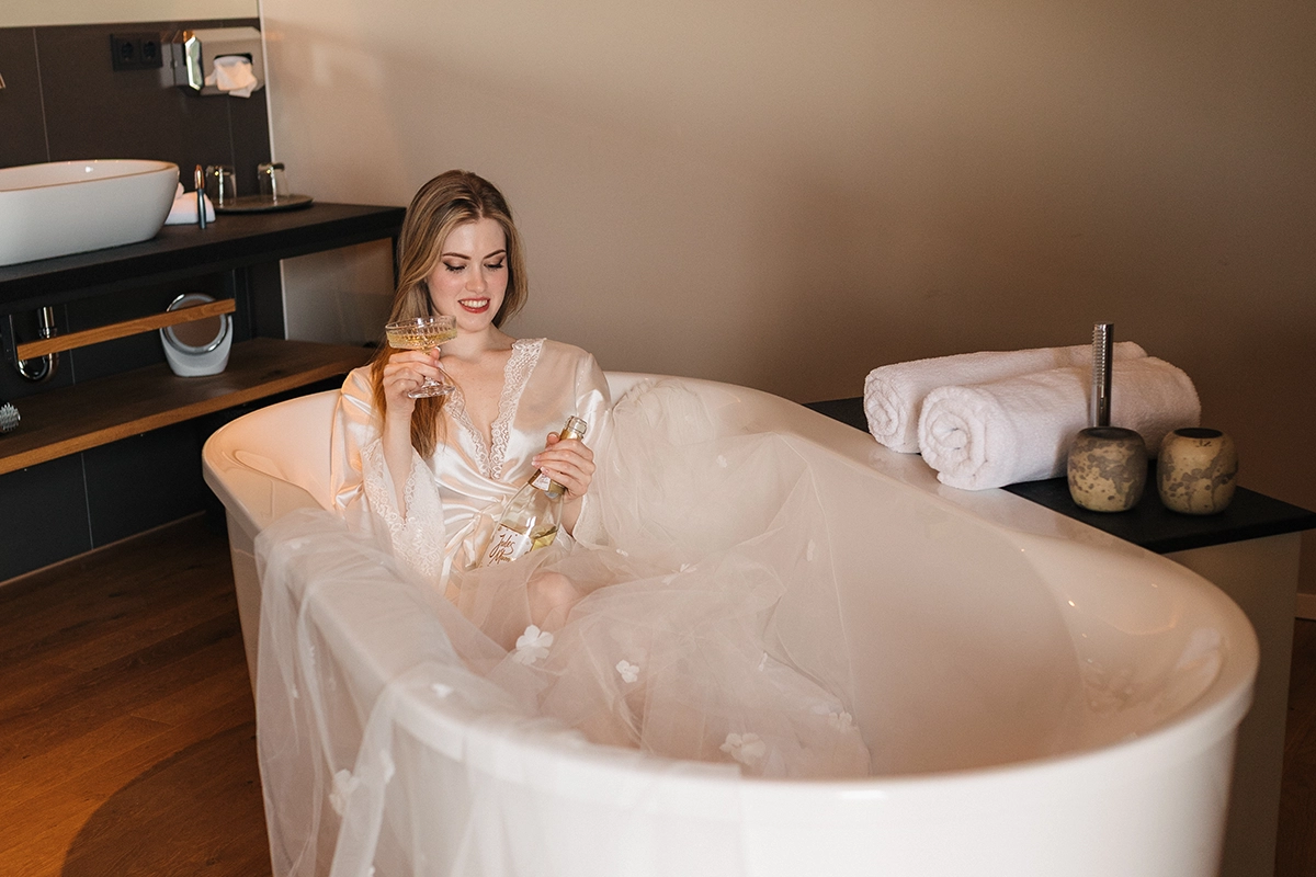 Frau mit einem Sektglas in der Badewanne während eines Bridal-Boudoir-Shootings