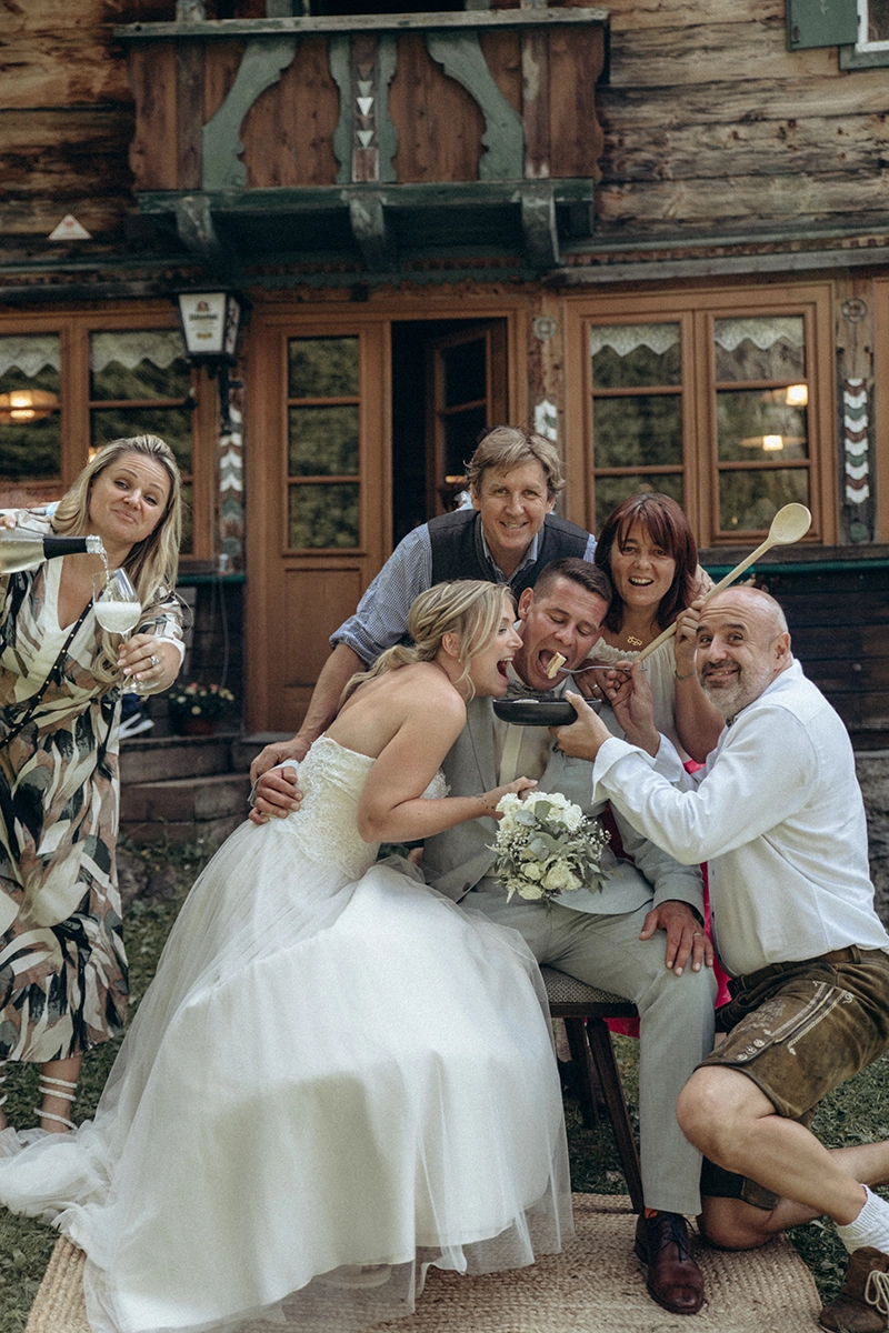 Das Brautpaar und beteiligte Dienstleister bei einem humorvollen Gruppenbild vor der Grawandhütte.