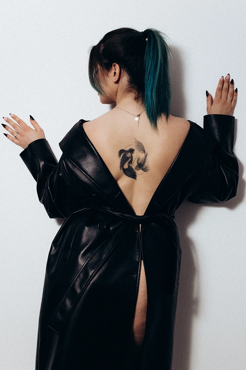 Rückenansicht einer Frau im geöffneten schwarzen Ledermantel mit sichtbarem Tattoo.